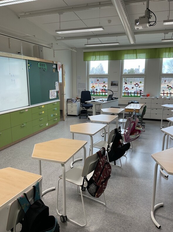 Avara luokkahuone valkoisine seinineen ja isoine ikkunoineen. 